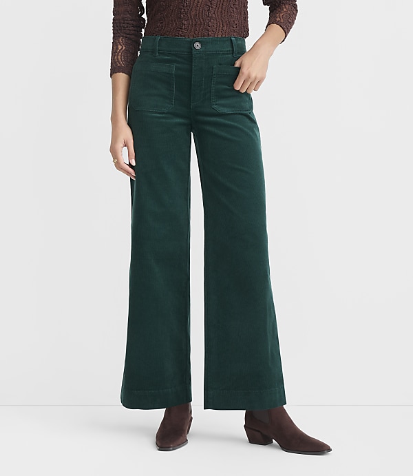 A person stands in front of a white background, wearing wide-leg green corduroy pants and brown boots.