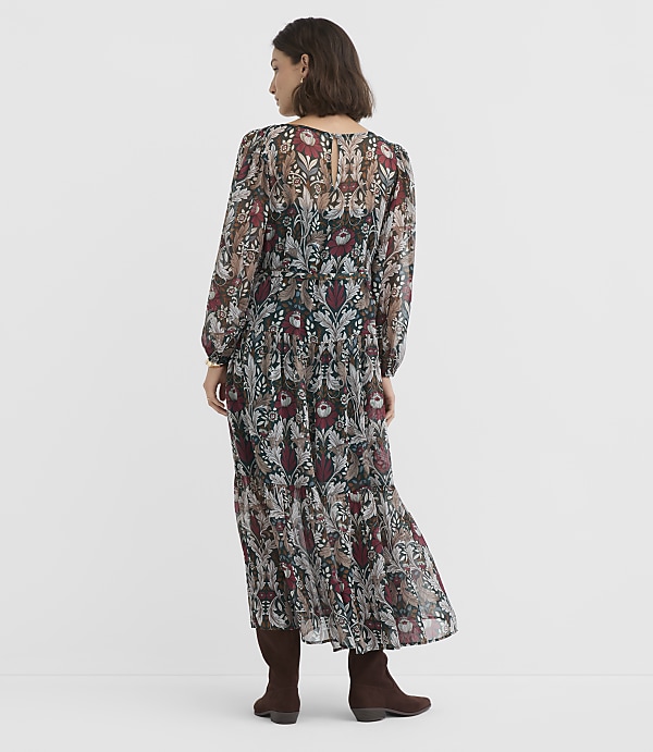 A woman in a floral print dress and brown boots stands against a plain white background.