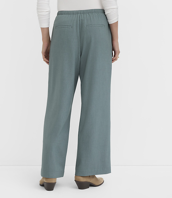 A person wearing teal wide-leg pants and tan boots stands against a plain white background.