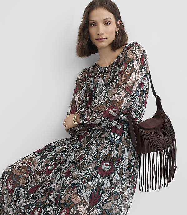 A woman in a floral dress with a fringed bag poses against a plain background.