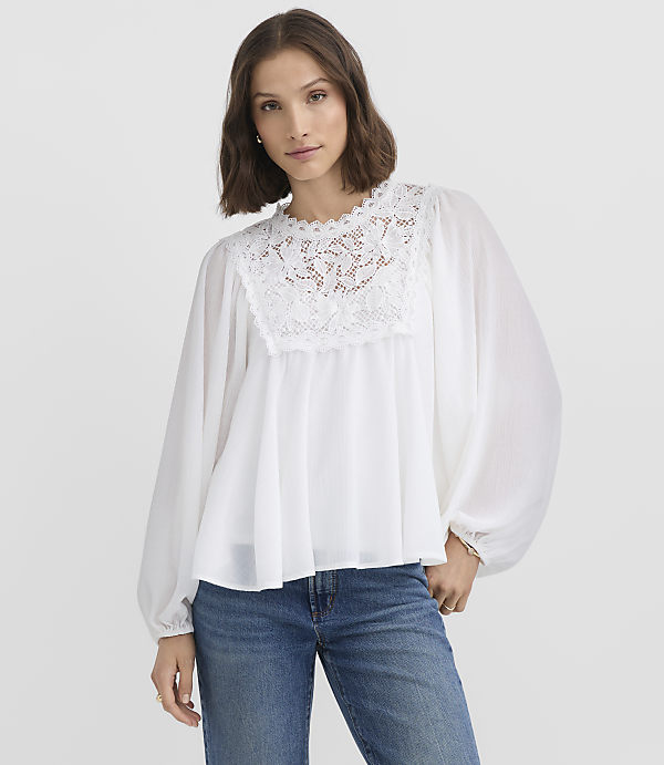 A woman in a white lace-trimmed blouse and blue jeans stands against a plain white background.