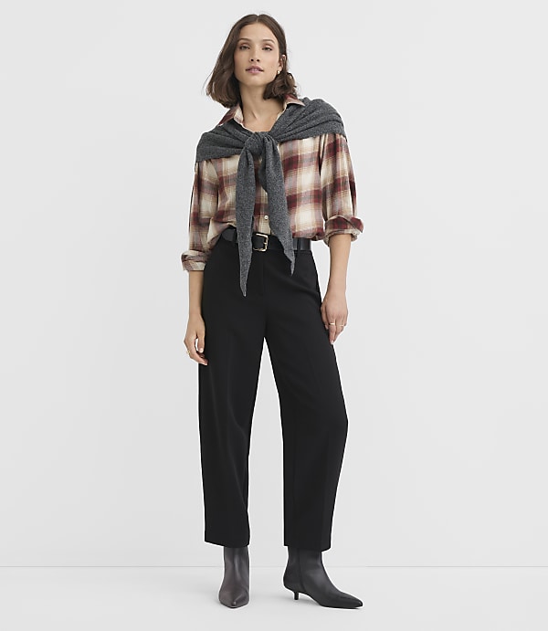 A woman in a plaid shirt and black pants stands against a plain white background.