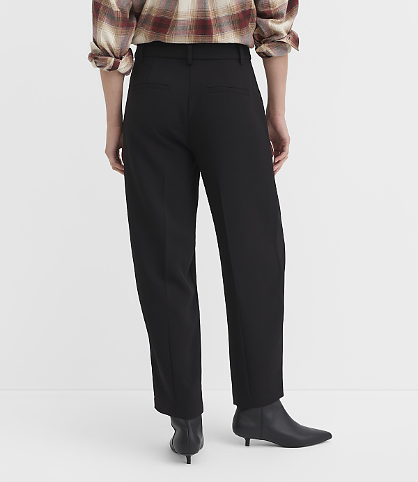 A person wearing black pants and a plaid shirt stands against a plain white background.
