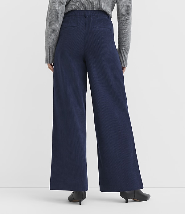 A person wearing wide-leg navy pants and a grey sweater stands against a plain white background.
