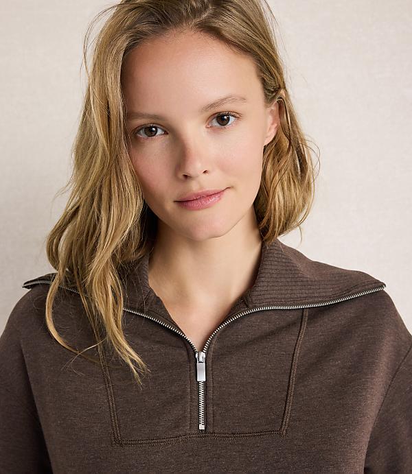 A young woman with blonde hair and a brown zippered sweatshirt is shown against a textured, light-colored background.