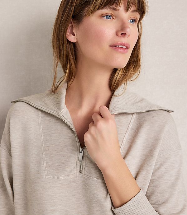 A woman in a beige quarter-zip sweatshirt looks off to the side against a neutral, textured background.