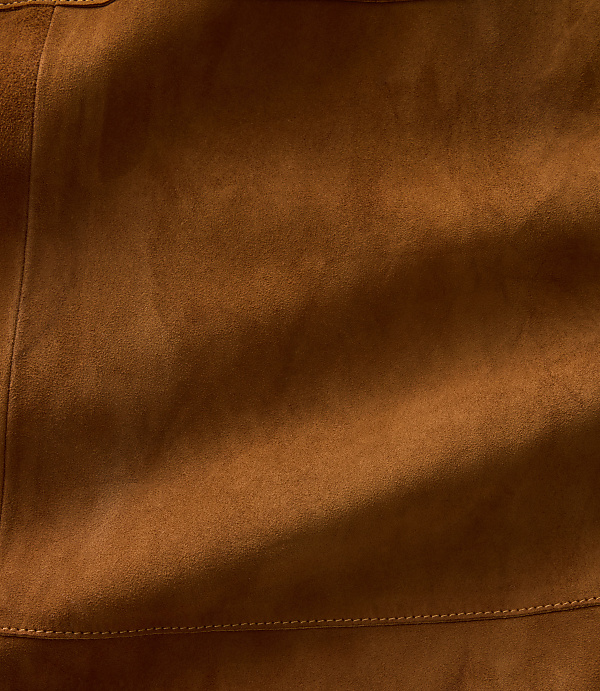 A close-up of textured brown suede with soft shadows and a stitched seam in the background.