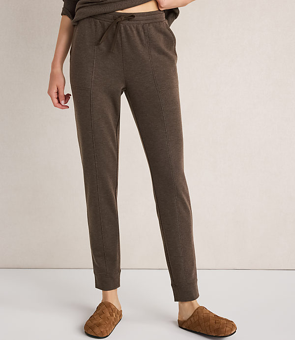 A person wearing brown loungewear pants and slippers stands against a plain white background.