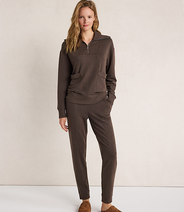 A woman in a brown loungewear set stands against a plain, light-colored background.