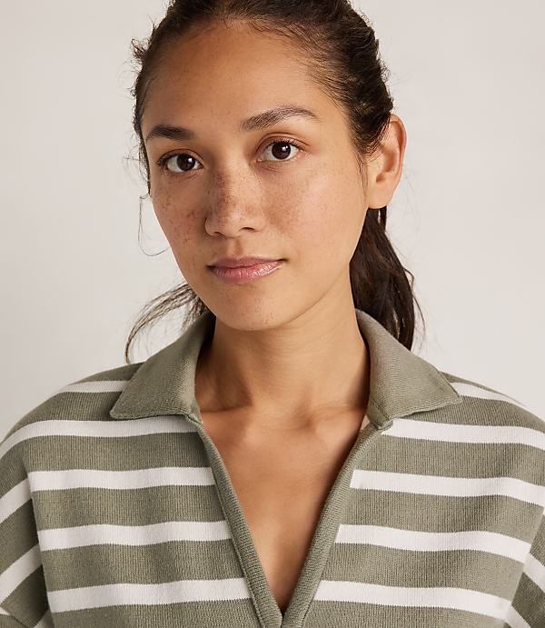 A woman with freckles and dark hair pulled back wears a green and white striped collared shirt against a plain, light background.
