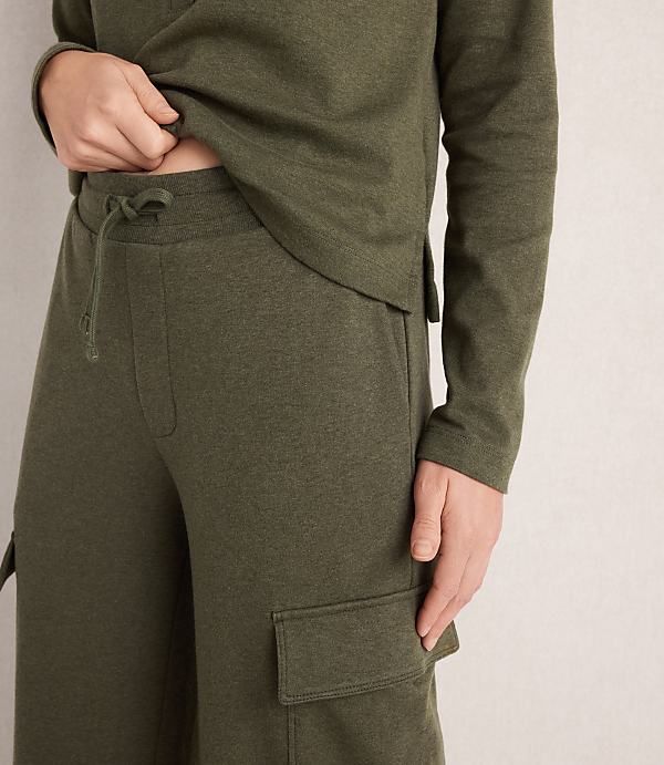 A person in a green loungewear set with cargo pockets stands against a textured, light-colored wall.