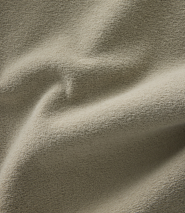 A close-up view of a textured, beige fabric with soft folds and shadows fills the frame.