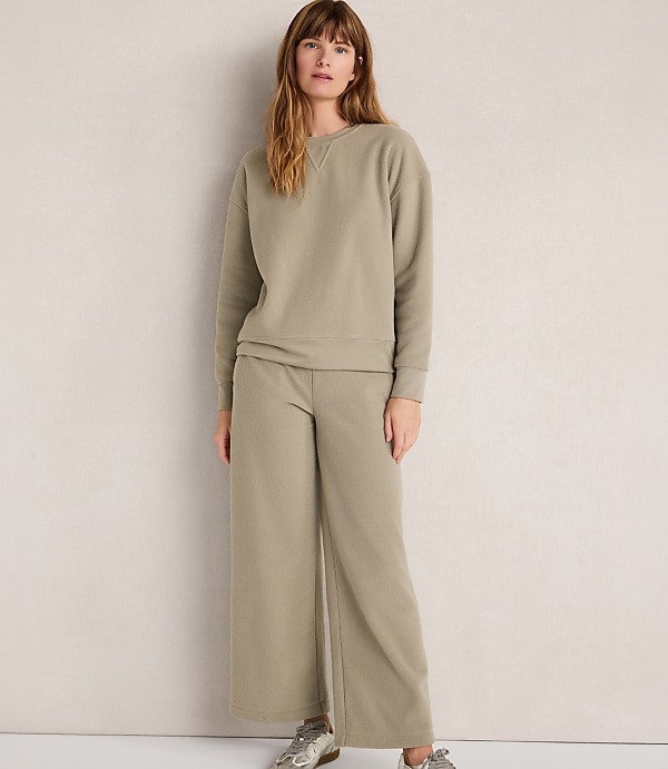 A woman in a light green loungewear set stands against a plain, textured gray background.