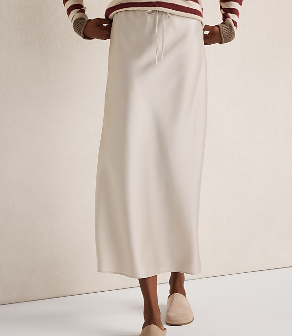 A person in a cream-colored slip skirt and a striped sweater stands against a plain, light-colored background.