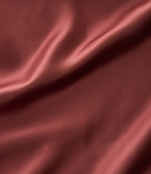 A close-up of rust-colored satin fabric with soft folds and highlights fills the frame.