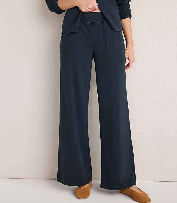 A person wearing dark blue wide-leg pajama pants and brown slippers stands against a plain, light-colored background.