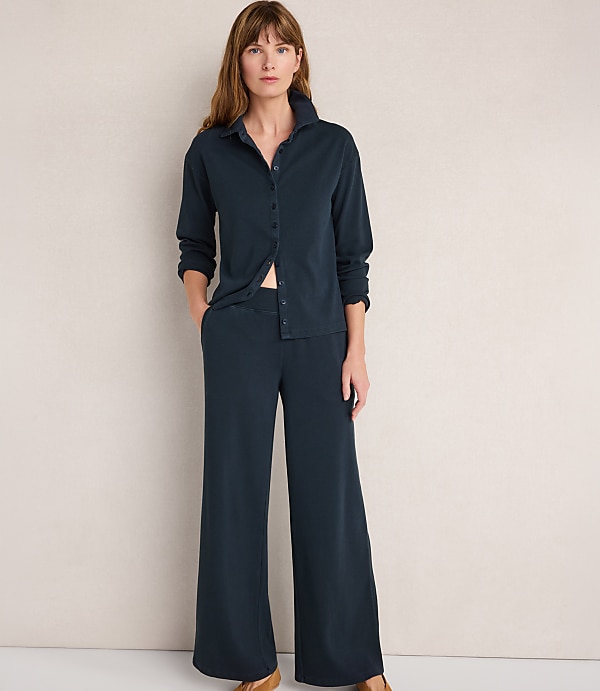 A woman in a dark blue pajama set stands against a plain, light-colored wall.