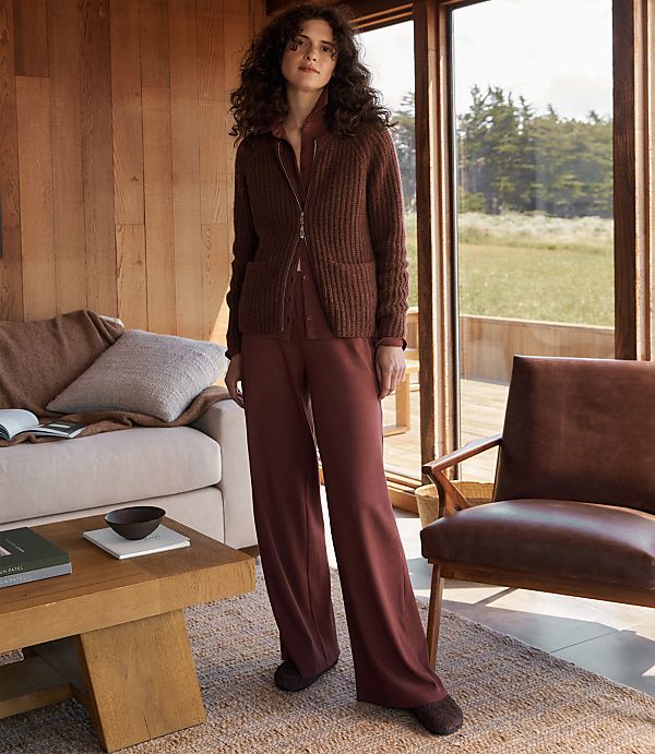 A woman stands in a cozy living room with a large window overlooking a grassy field.