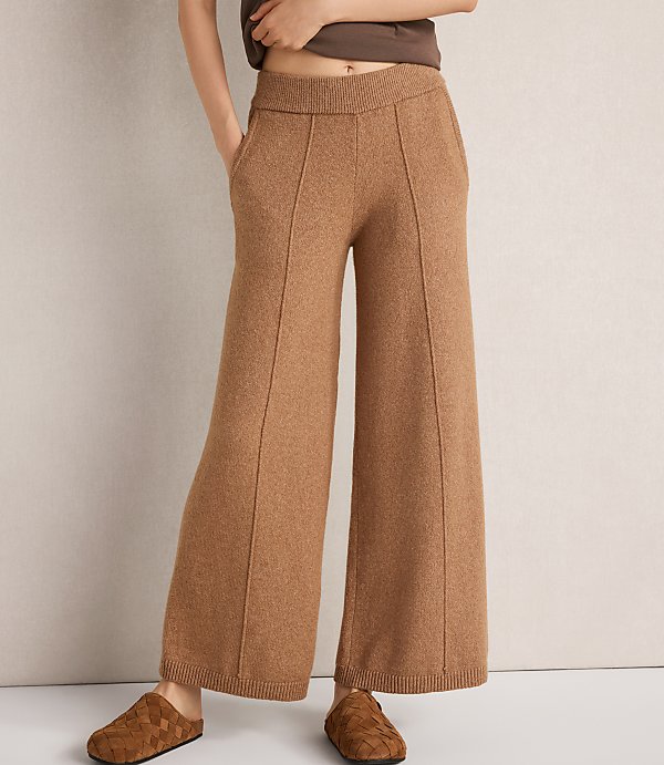 A person models wide-leg, camel-colored knit pants with pockets and a plain background.