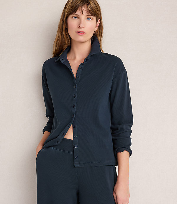 A woman in a dark blue ribbed shirt and pants stands against a plain, light-colored background.