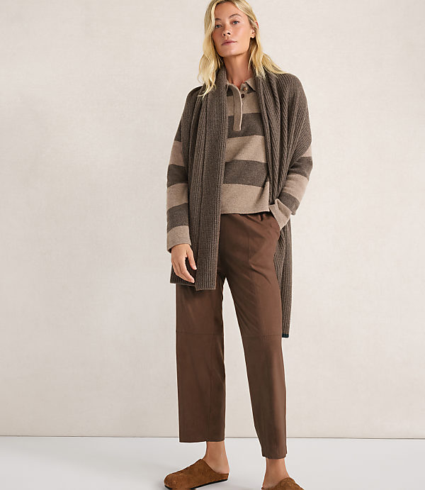 A woman in a brown striped sweater, brown pants, and a brown cardigan stands against a plain beige background.