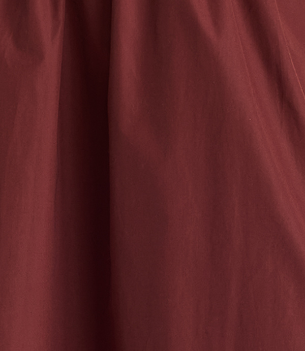 A close-up of a deep red, textured fabric fills the frame, with soft folds creating subtle shadows and highlights.