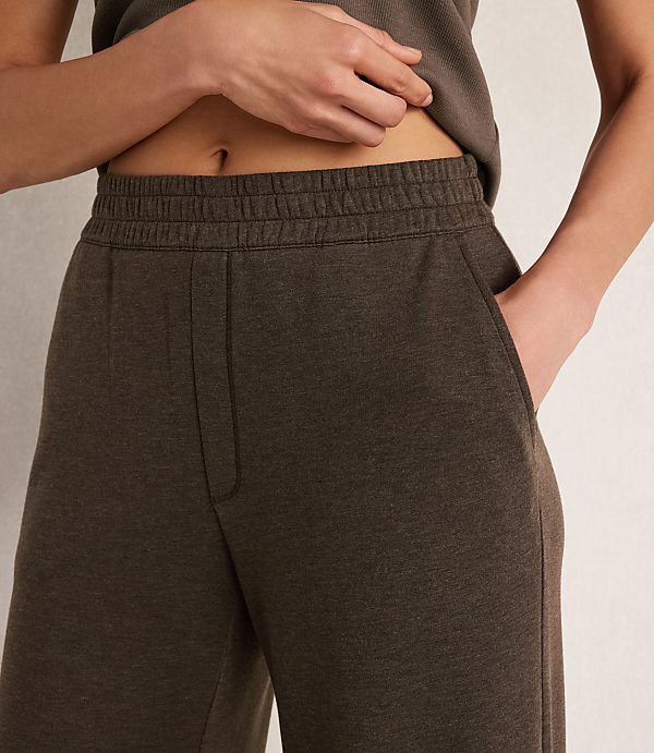 A person's torso, wearing a dark grey tank top and matching sweatpants with a hand in one pocket, is shown against a plain, light background.