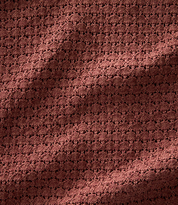A close-up view of a textured, reddish-brown knitted fabric with a subtle shadow cast across its surface.