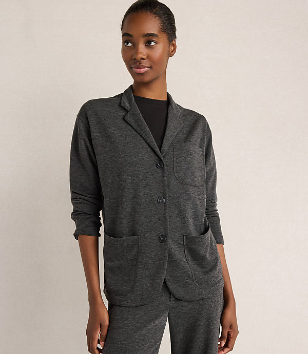 A woman in a dark grey cardigan stands against a plain, light grey background.