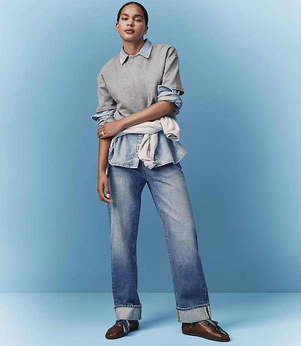A woman in a grey sweatshirt and jeans stands against a bright blue background.