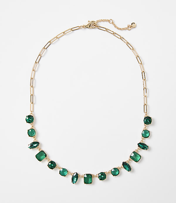 A gold chain necklace with various green gemstones is displayed against a plain white background.