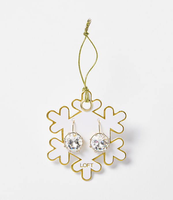 A pair of sparkling crystal earrings hang from a gold string attached to a white snowflake ornament with gold trim, set against a plain white background.