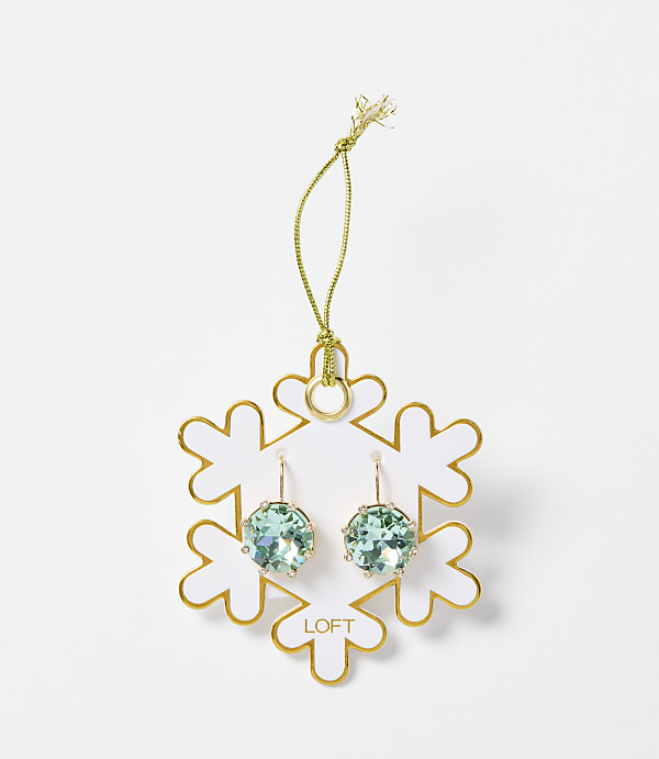 A pair of light blue crystal earrings hang from a gold string attached to a white snowflake ornament with gold trim, set against a plain white background.