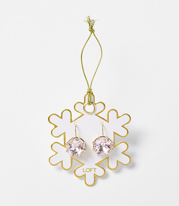 A pair of pink crystal earrings hangs from a gold string attached to a white snowflake ornament with gold trim, set against a plain white background.