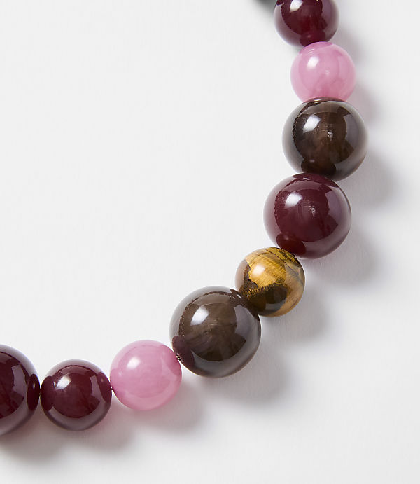 A close-up of a bracelet with various colored beads, including pink, deep red, and tiger's eye, is set against a plain white background.