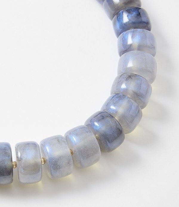 A bracelet of translucent, blue-grey beads with iridescent flashes is displayed against a plain white background.