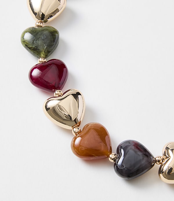 A string of colorful heart-shaped beads, ranging from gold to dark purple, is laid out against a plain white background.