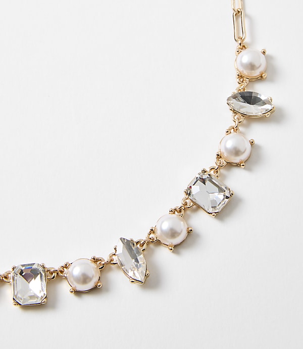 A delicate gold necklace with pearls and clear gemstones is displayed against a plain white background.