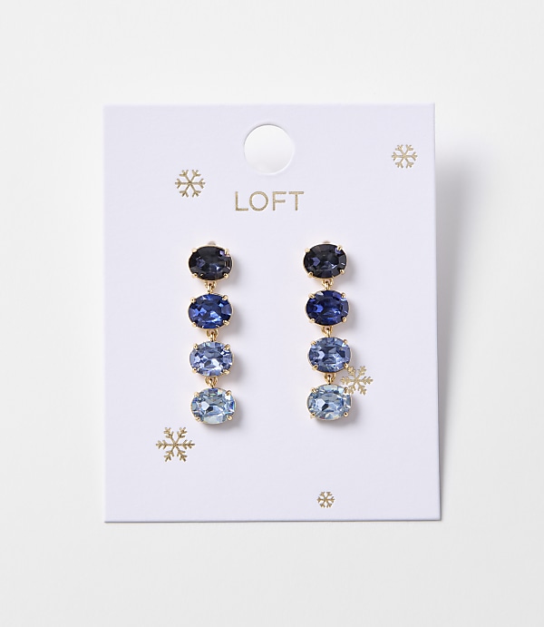 A pair of blue gemstone drop earrings with gold accents hangs from a white card with snowflake designs and the "LOFT" logo.