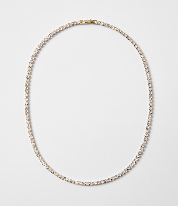 A delicate gold chain necklace with clear stones is laid out on a plain white background.