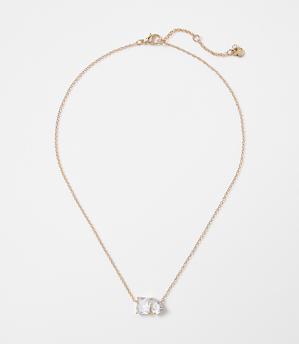 A delicate rose gold necklace with two clear, rectangular stones rests on a plain white background.