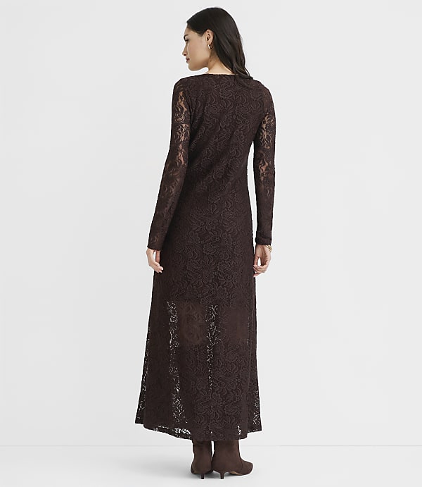 A woman in a long-sleeved brown lace dress stands against a plain white background.