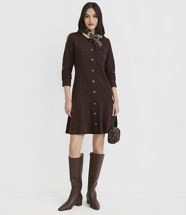 A woman in a brown knit dress, knee-high boots, and a patterned scarf stands against a plain white background.