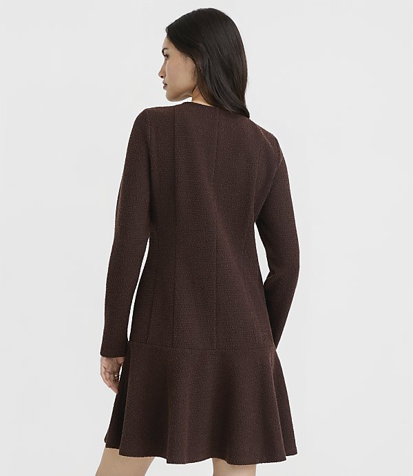 A woman in a brown textured dress stands against a plain white background.