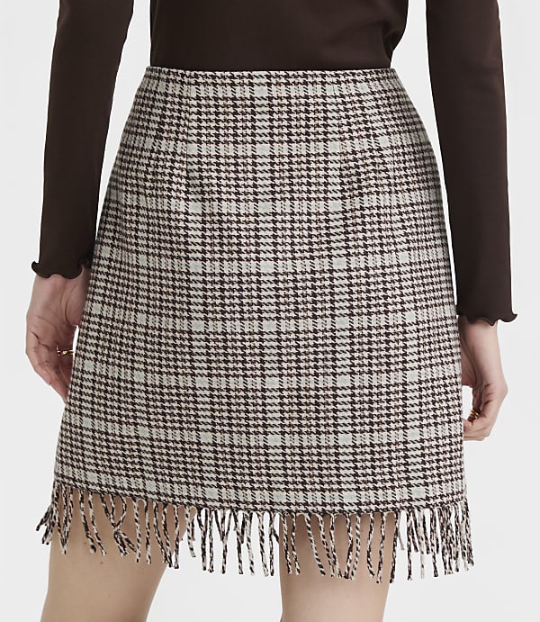 A brown and white plaid mini skirt with fringe detail is worn by a person against a plain background.