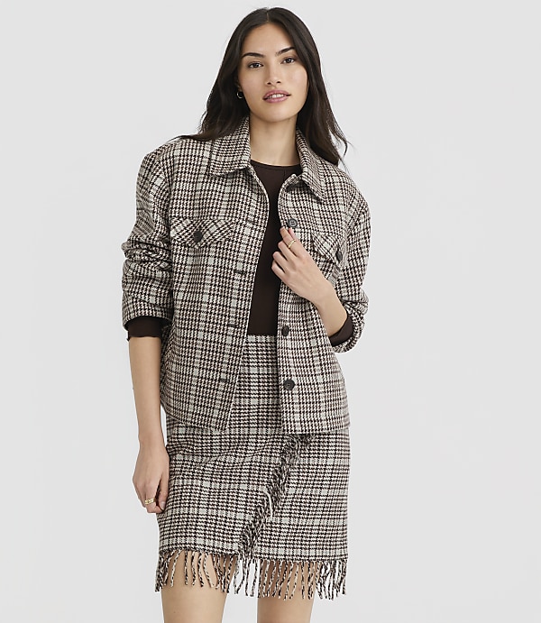 A woman in a plaid jacket and skirt stands against a plain gray background.