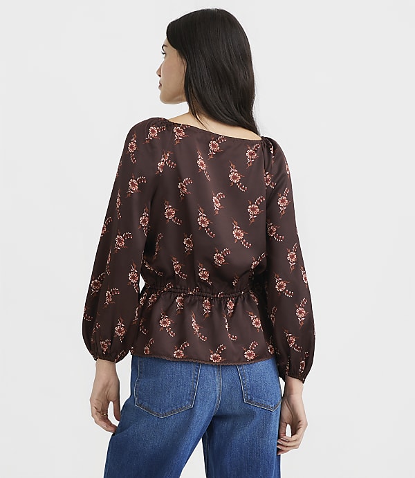 A woman in a floral print blouse and jeans stands against a plain white background.