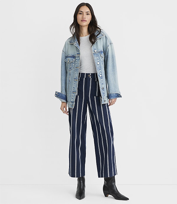 A woman in a denim jacket and striped pants stands against a plain white background.