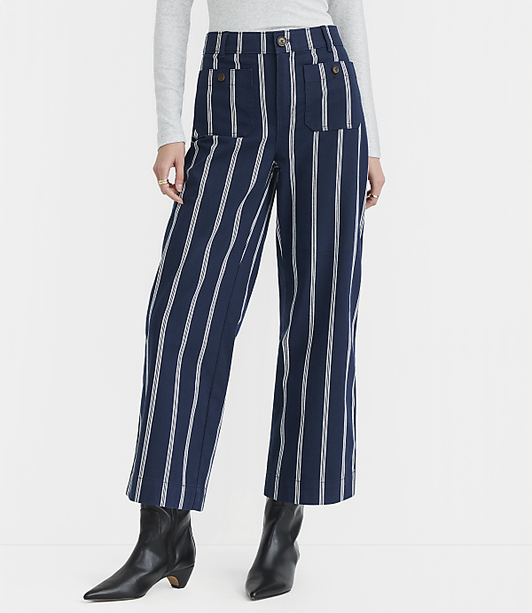 A person stands in front of a plain white background, wearing navy and white striped wide-leg pants and black boots.