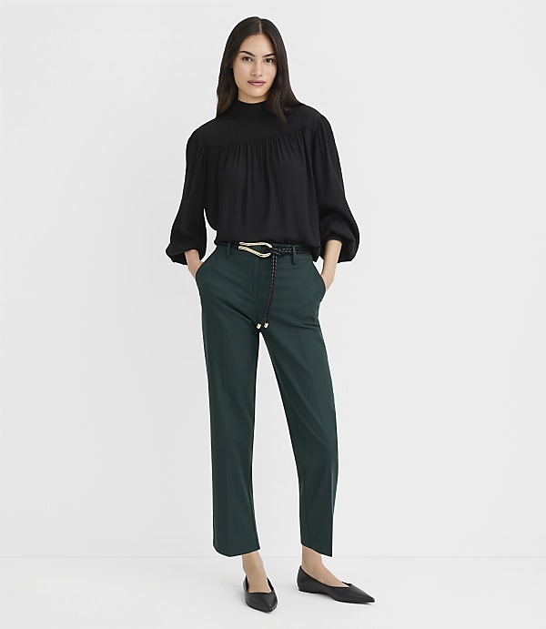 A woman in a black blouse and green pants stands against a plain white background.